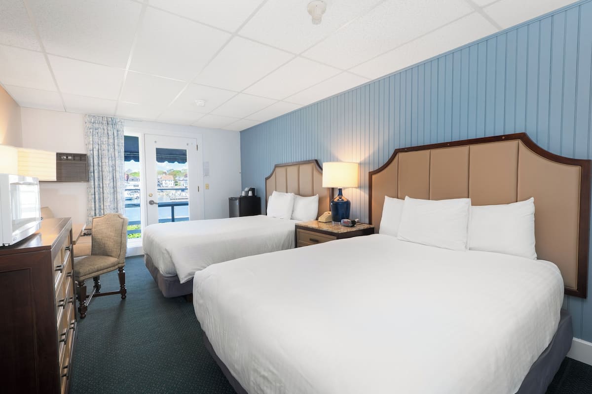 A hotel room with two beds, a desk, a chair, and a window with a view of the outside.