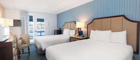 A hotel room with two beds, a desk, a chair, and a window with a view of the outside.