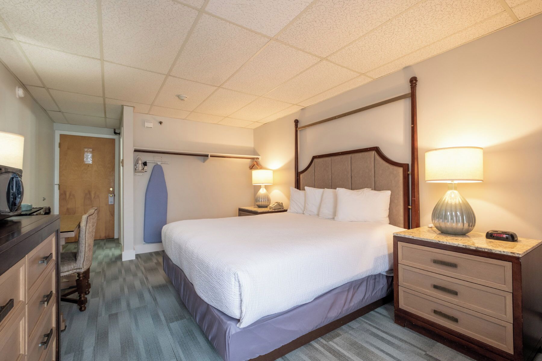 A hotel room with a large bed, bedside tables with lamps, a dresser, and a door leading to a closet.