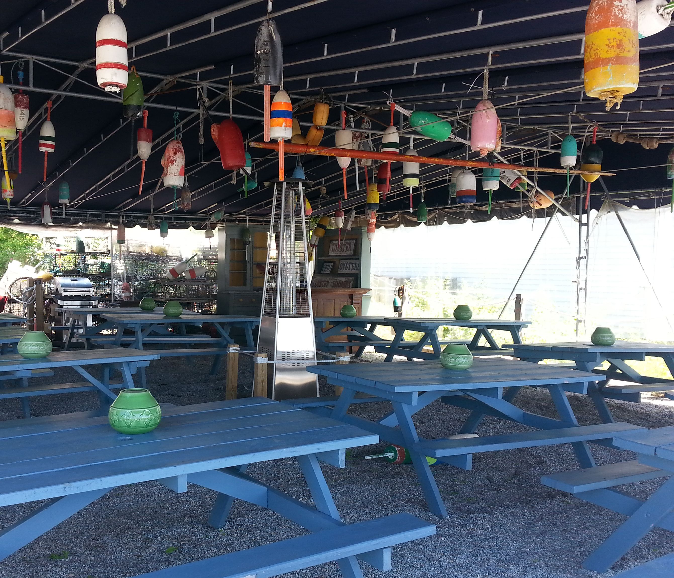 Un área de estar al aire libre con mesas y sillas azules, decorada con boyas de colores y un letrero que dice 'TOASTER OYSTERS'.