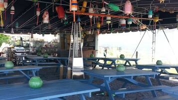 Un área de estar al aire libre con mesas y sillas azules, decorada con boyas de colores y un letrero que dice 'TOASTER OYSTERS'.