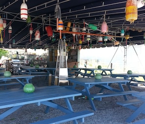 An outdoor seating area with blue tables and chairs, decorated with colorful buoys and a sign indicating 'TOASTER OYSTERS'.