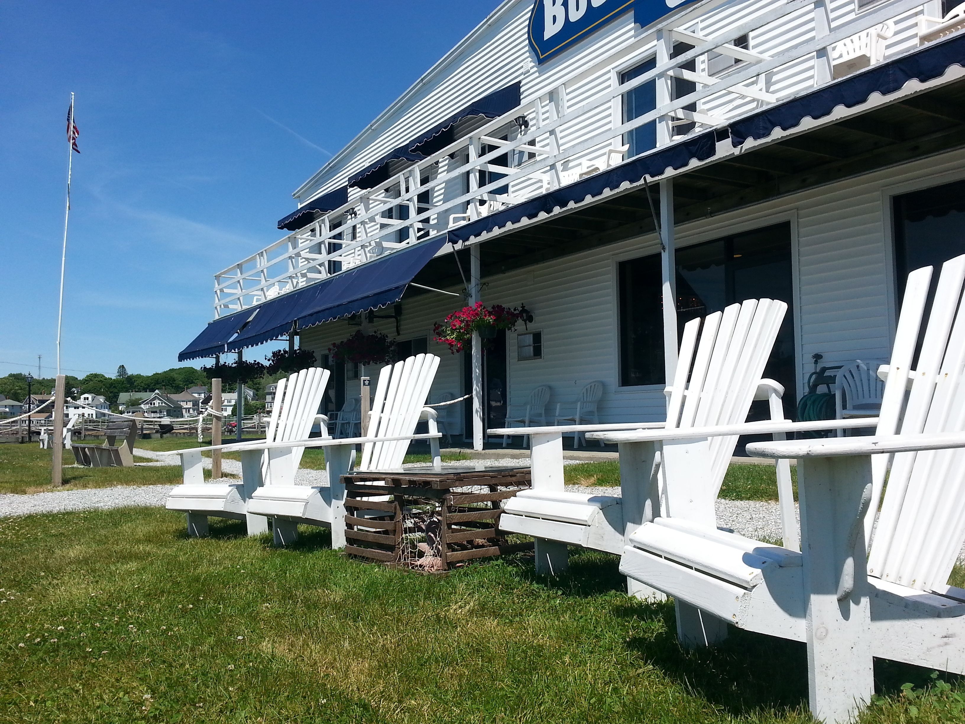 A building with a blue sign reading "BUDS" and white exterior. There are white Adirondack chairs arranged outside.