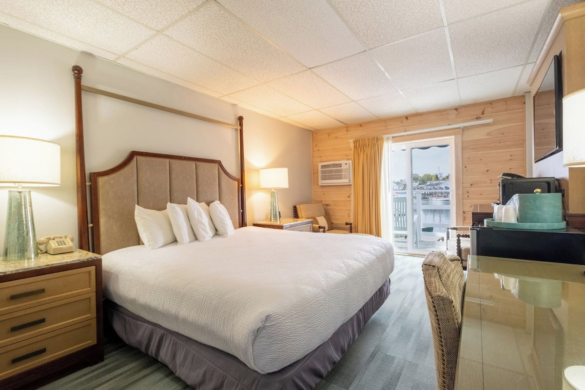 A hotel room with a bed, bedside tables, a desk, a chair, and a view of the outside.