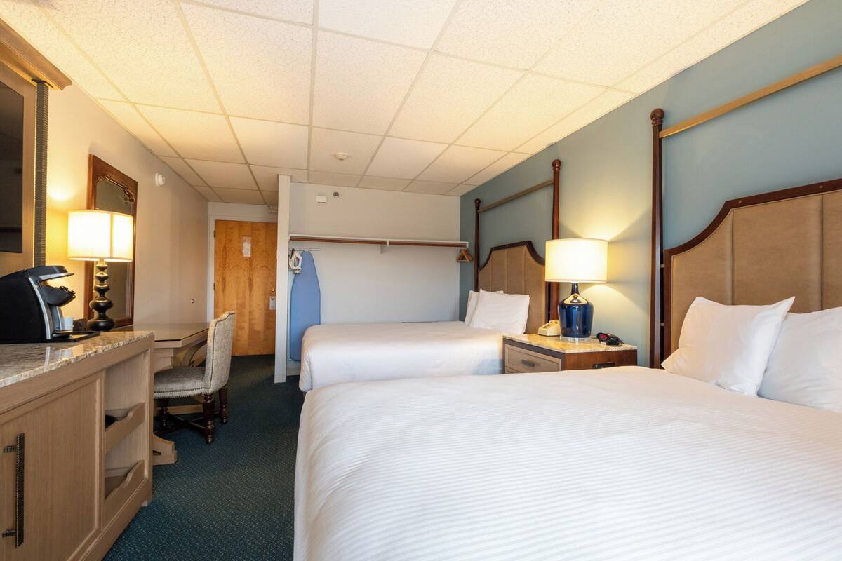 A hotel room with two beds, a desk with a telephone, a chair, and a mirror.