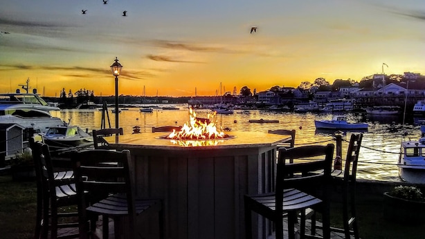 A waterfront dining area with a fire feature, boats, and a sunset view. - Boothbay Harbor Inn (Boothbay Harbor)