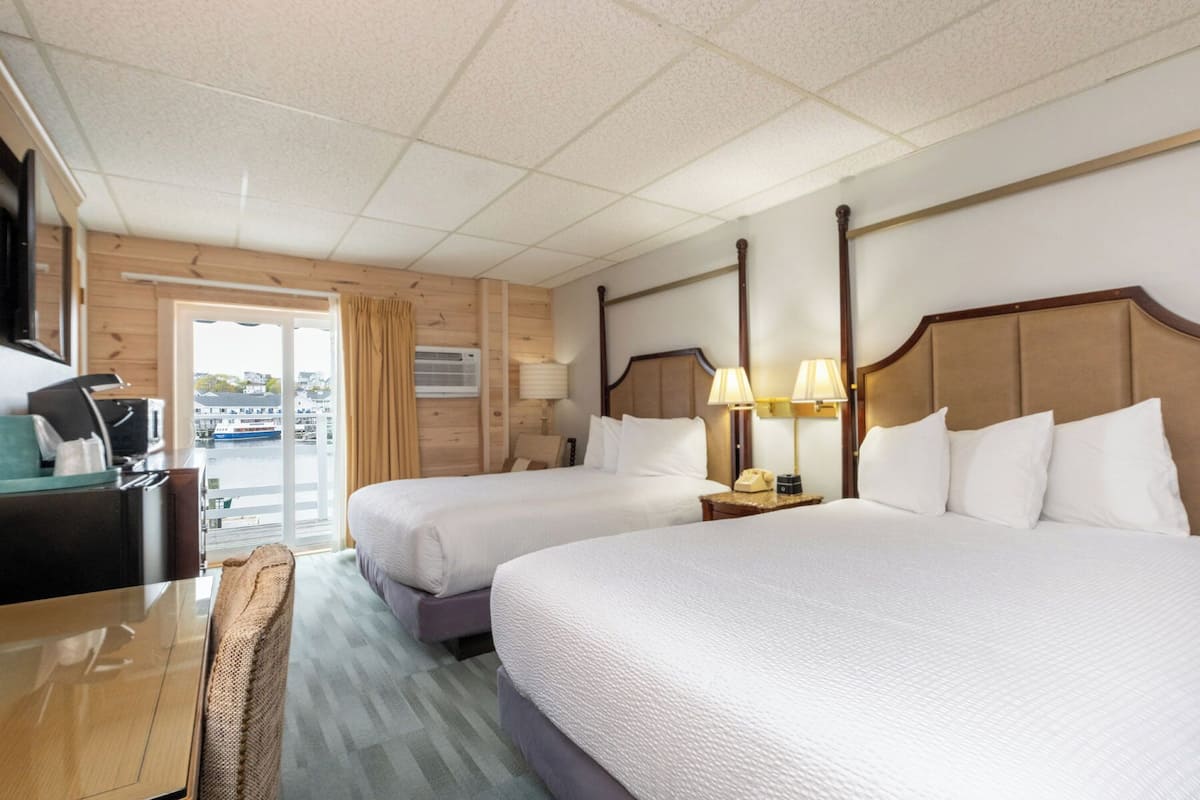 A hotel room with two beds, a desk, a television, and a view of the outside.