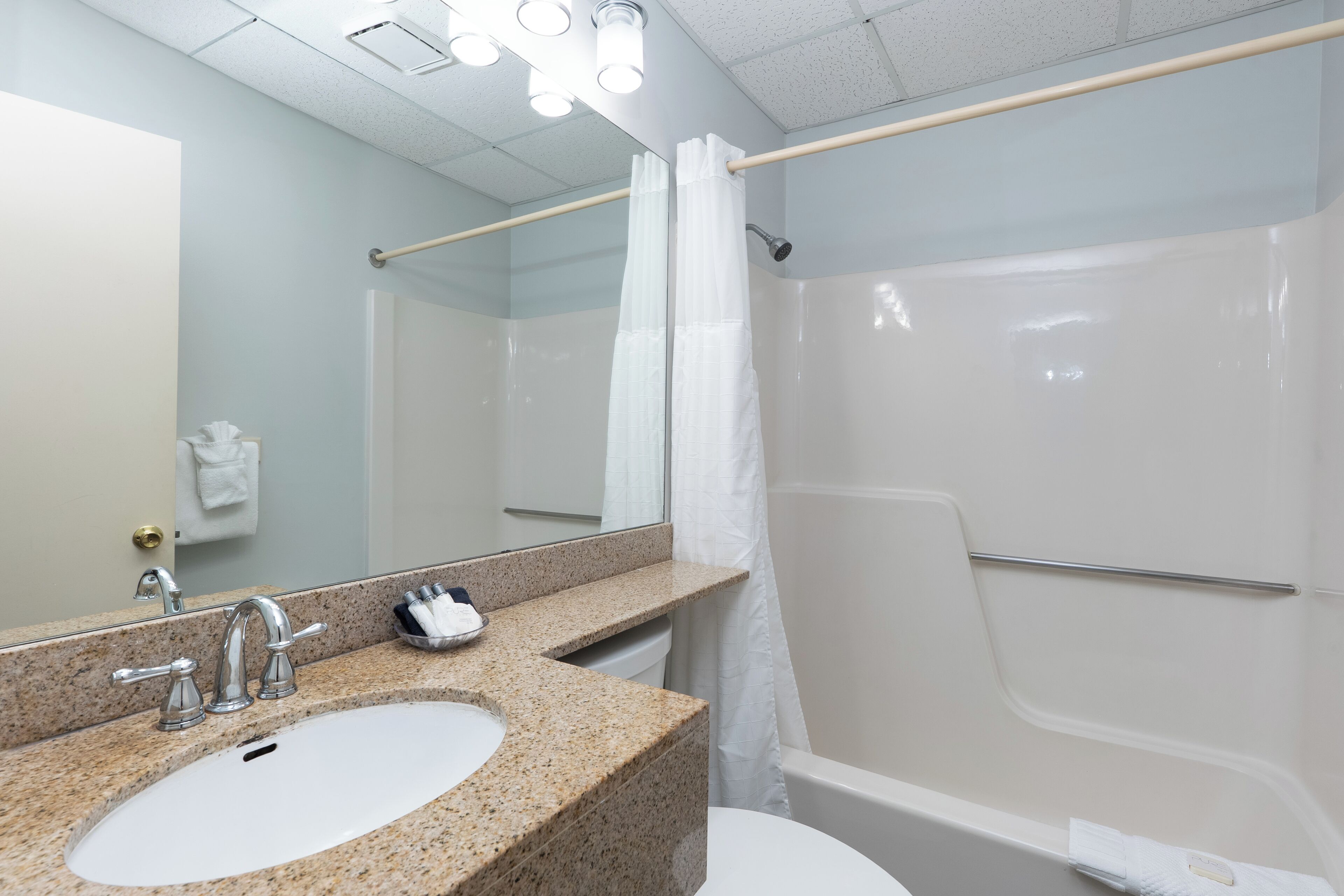 A bathroom with a granite countertop sink, a mirror, a shower with a curtain, and a towel rack.