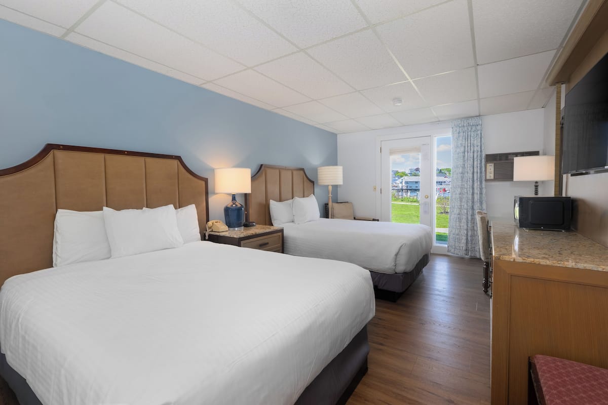 A hotel room with two beds, a TV, a desk, and a view of the outdoors.