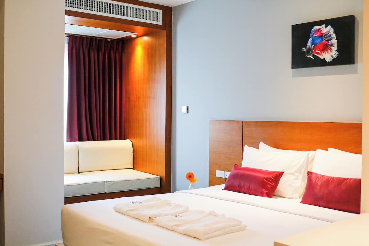 Una habitación de hotel con cama, una zona de estar con cortina, un cuadro en la pared y un pequeño jarrón con una flor.