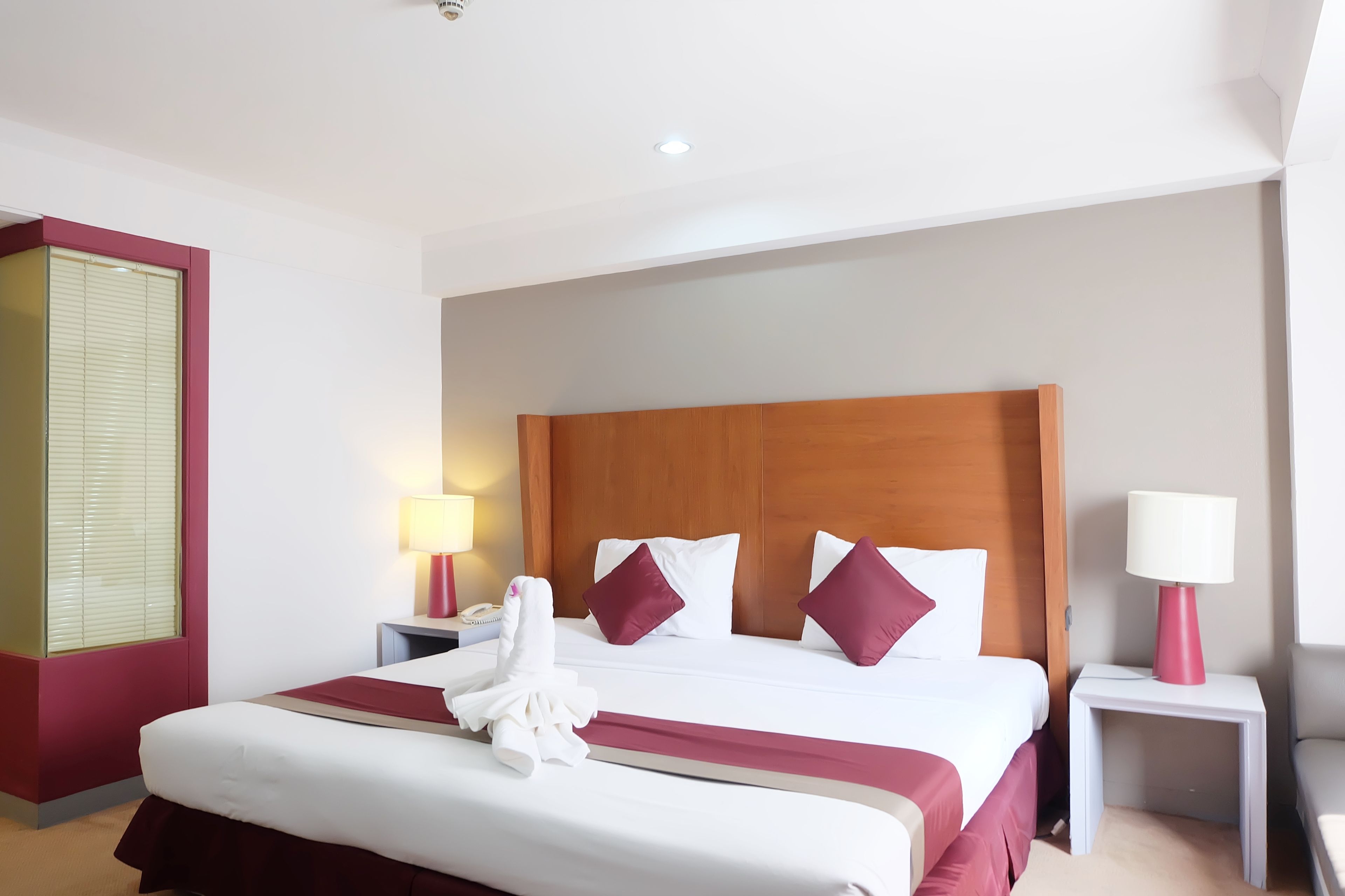 Ein Hotelzimmer mit einem großen Bett, zwei Nachttischen, einem Holzkopfstück und einem Fenster mit Jalousien.