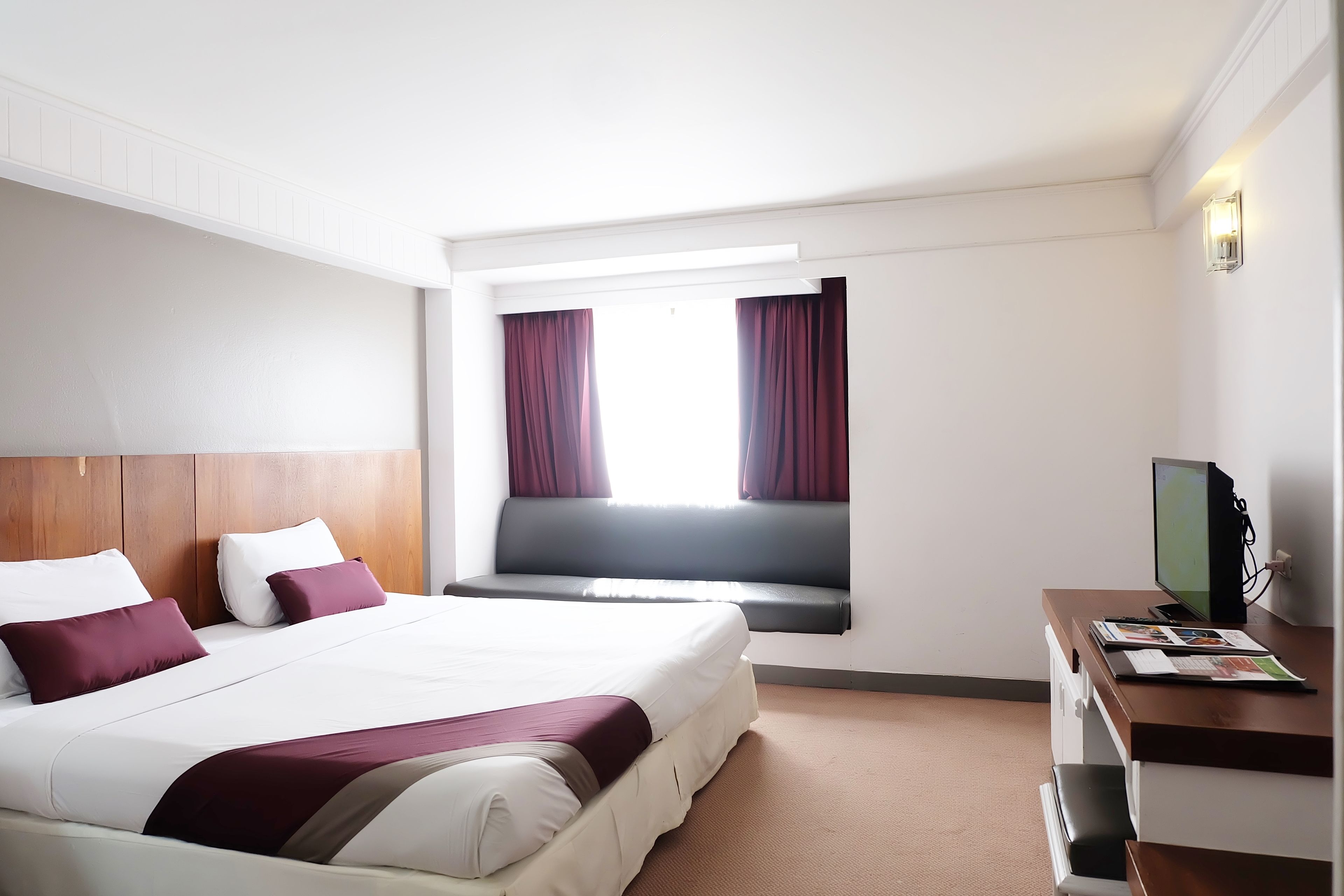Een hotelkamer met een groot bed, een bureau met een computer en een raam met gordijnen.