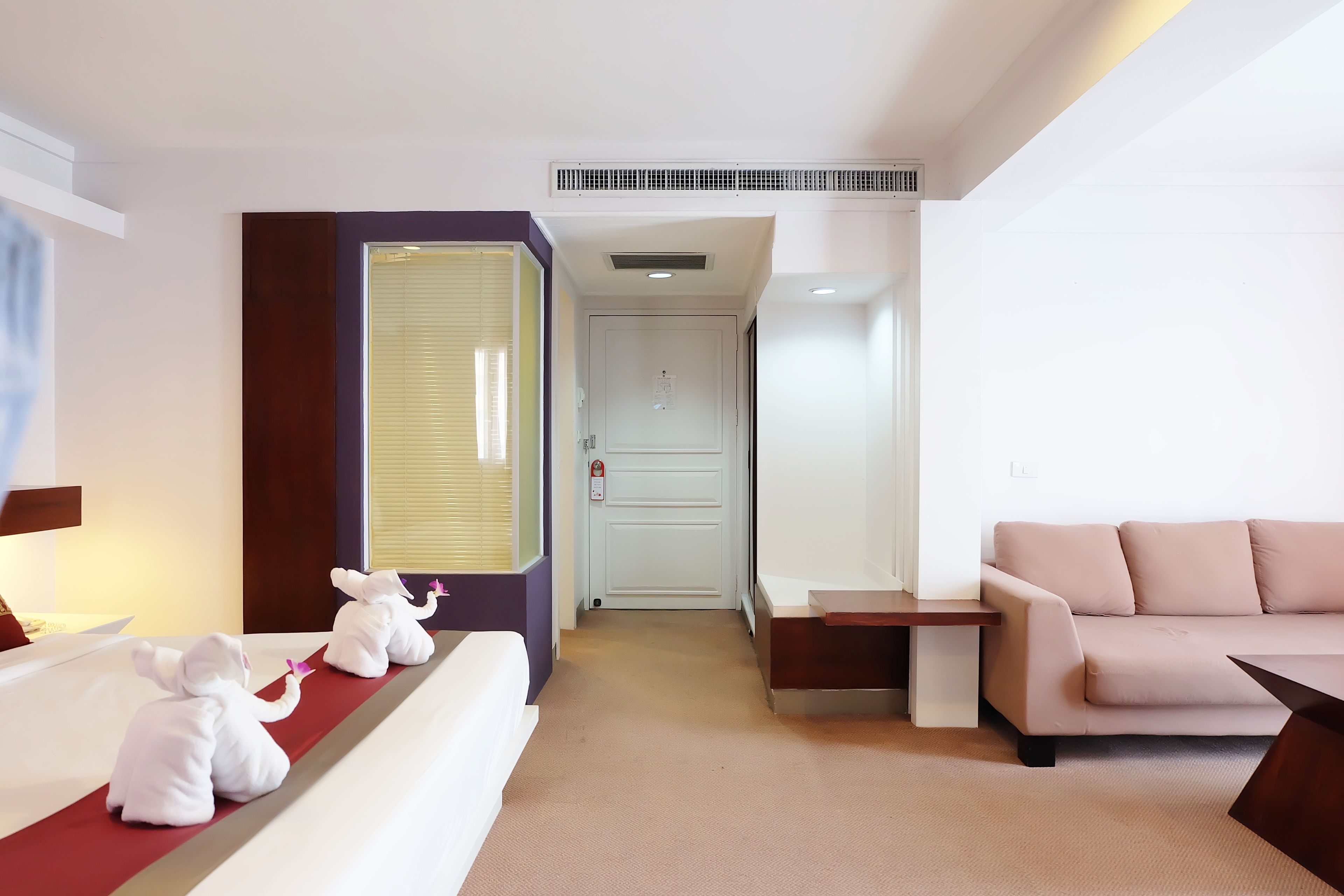 A hotel room with a bed, a sofa, a small table, and a window with blinds.