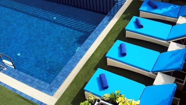 Piscina con sillones reclinables azules y una pequeña zona junto a la piscina con plantas.