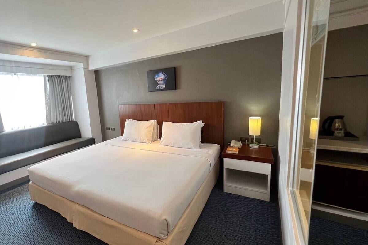 Un cuarto de hotel con una cama grande, una mesita de noche con lámpara, una ventana con cortinas y un cuadro en la pared.