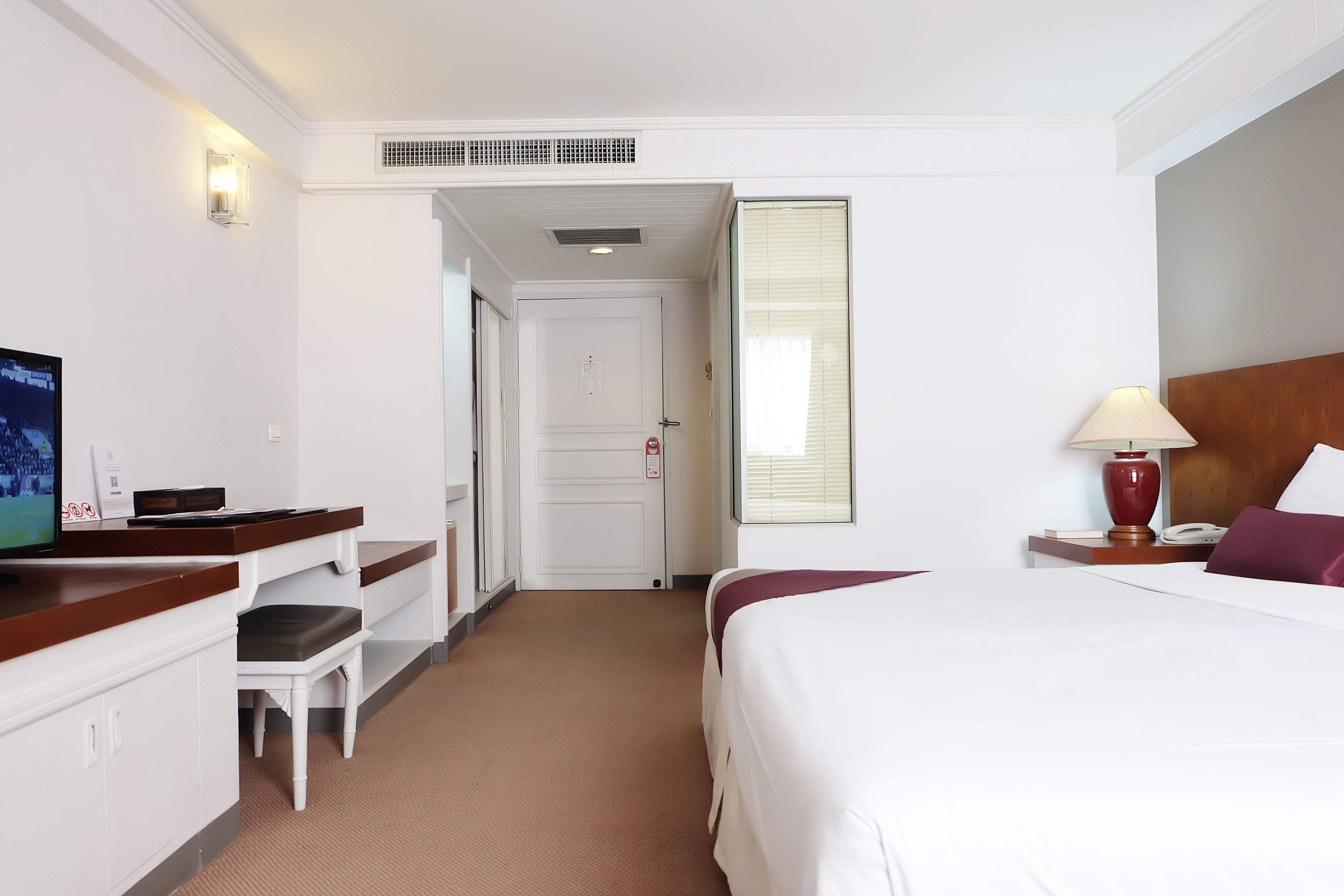 Una habitación de hotel con cama, escritorio con silla, televisor, lámpara y ventana con persianas.