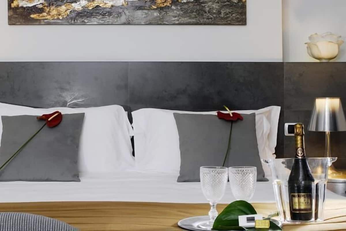 A neatly made bed with white linens, two red roses, and two clear glasses on a tray.