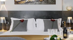 Una cama bien hecha con sábanas blancas, dos rosas rojas y dos vasos sobre una bandeja.