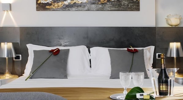 A neatly made bed with white linens, two red roses, and two clear glasses on a tray.