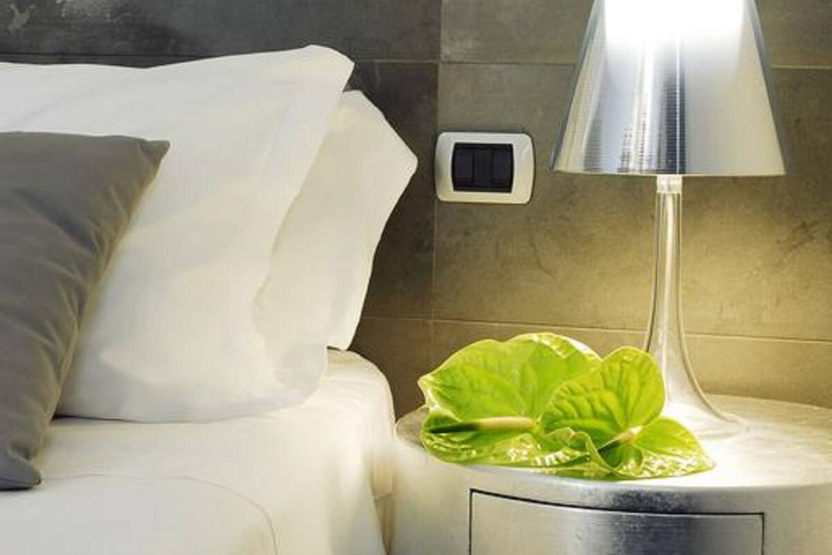A neatly made bed with white linens and a gray pillow, a modern lamp on a bedside table, and a small digital clock.