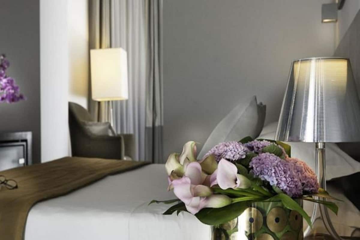 A hotel room with a neatly made bed, a bedside table with a lamp, and a vase of flowers.