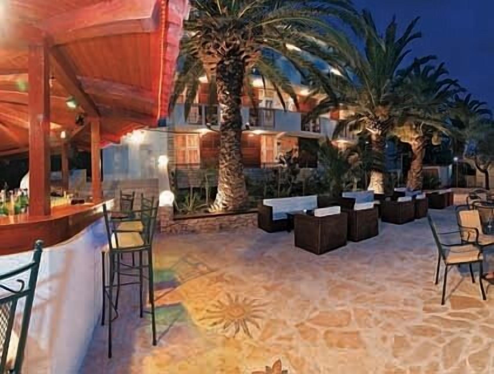 An outdoor bar area with seating, palm trees, and a stone floor.