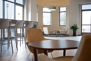A modern interior with a seating area featuring a round table and chairs, large windows, and a hanging light fixture. - Newport News Marriott at City Center (Newport News)