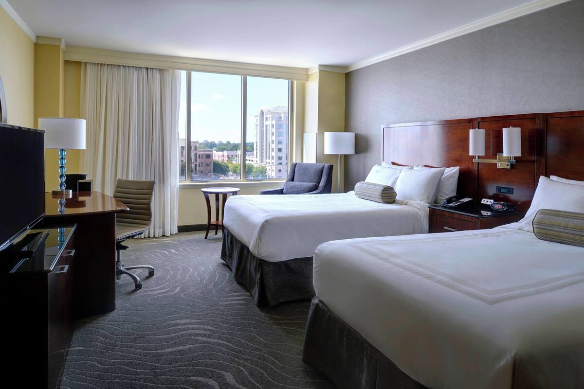 A hotel room with two beds, a desk, a chair, and a television.