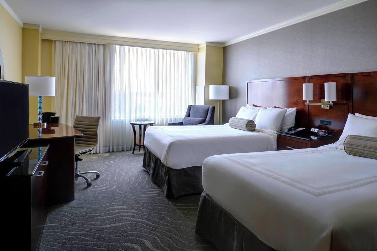 A hotel room with two beds, a desk with a computer, a chair, a small table, and a TV.