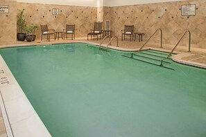 A swimming pool with a tiled wall, lounge chairs, and potted plants. - Newport News Marriott at City Center (Newport News)