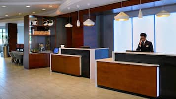 A hotel reception area with three wooden reception desks, a large plant, and a modern chandelier.