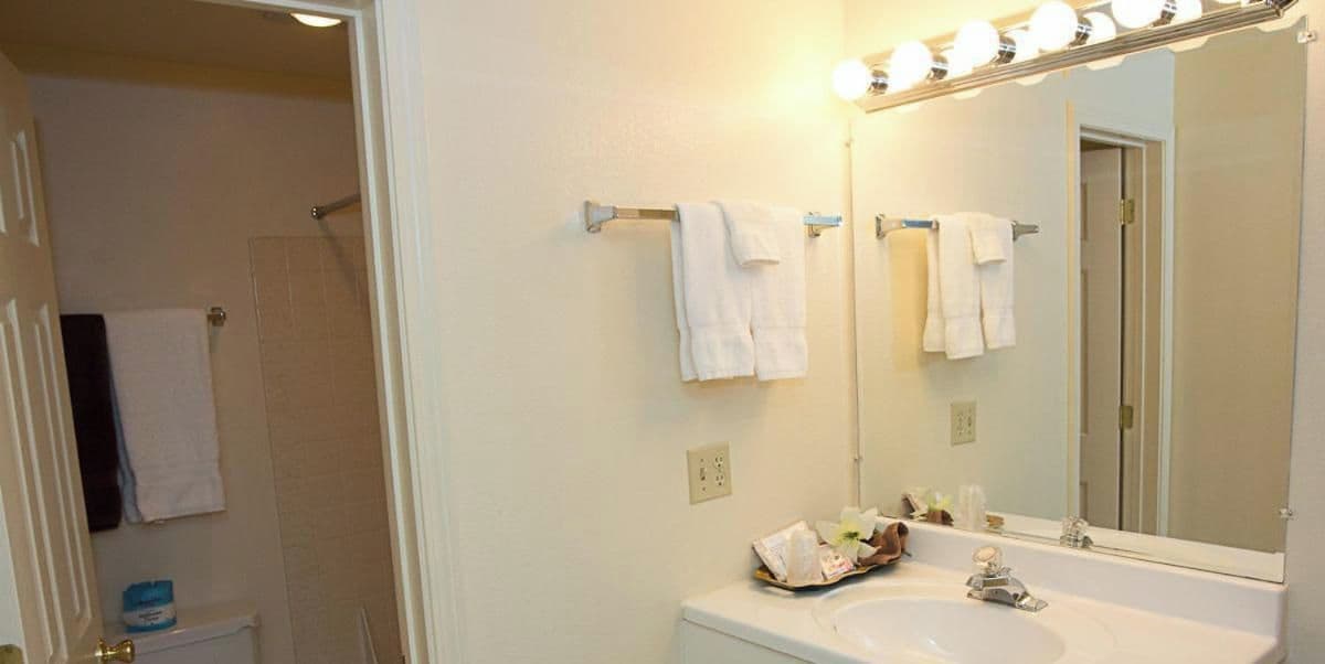 Un baño con lavamanos blanco, un espejo con iluminación y toallas colgadas en ganchos.
