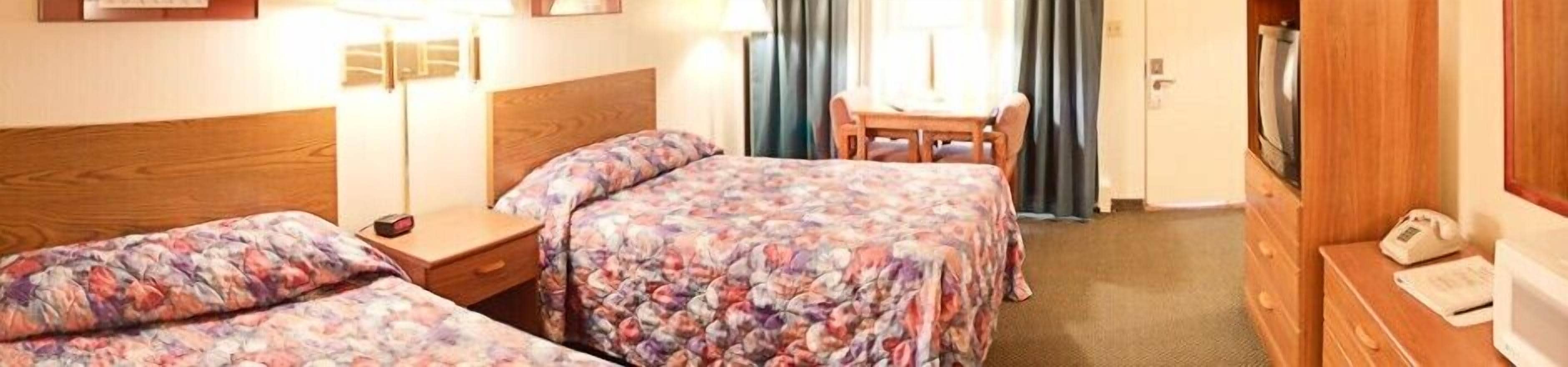 Habitación de hotel con dos camas, cabecero de madera, mesita de noche, una silla, escritorio y armario.