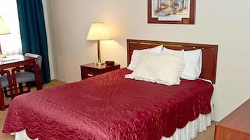 Habitación de hotel con cama, escritorio, silla, lámpara y un cuadro en la pared.