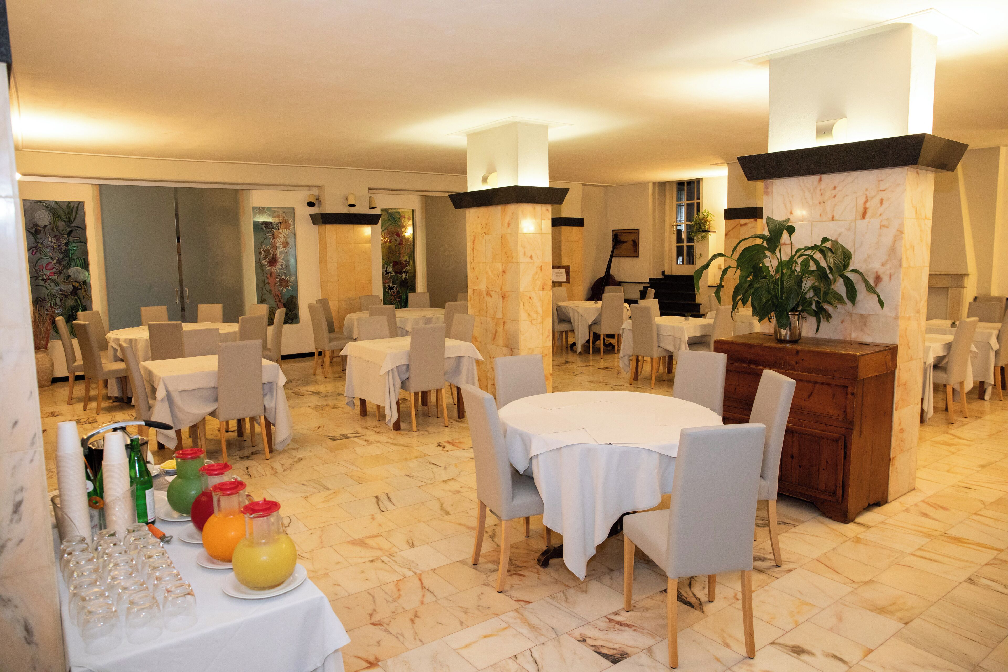 A spacious dining area with multiple round tables and chairs, a marble-tiled floor, and a central wooden counter.