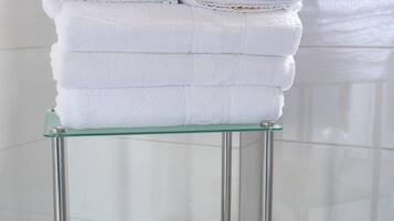 Una repisa de vidrio con toallas blancas dobladas, una cesta amarilla y un rollo de papel higiénico en un baño.