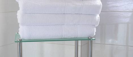 A glass shelf with folded white towels, a yellow basket, and a roll of toilet paper in a bathroom.