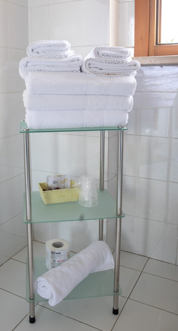 A glass shelf with folded white towels, a yellow basket, and a roll of toilet paper in a bathroom. - Hotel Park Ge. Al. (Città di Castello)