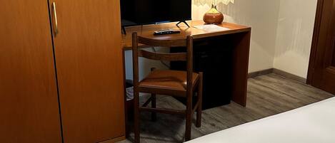 A hotel room with a bed, a desk with a lamp, a television, and a wardrobe.