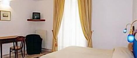 A hotel room with a bed, a desk, a chair, and a radiator.