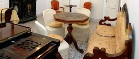 Ein Zimmer mit einem Klavier, einer Couch, einem kleinen runden Tisch und einem Sessel.