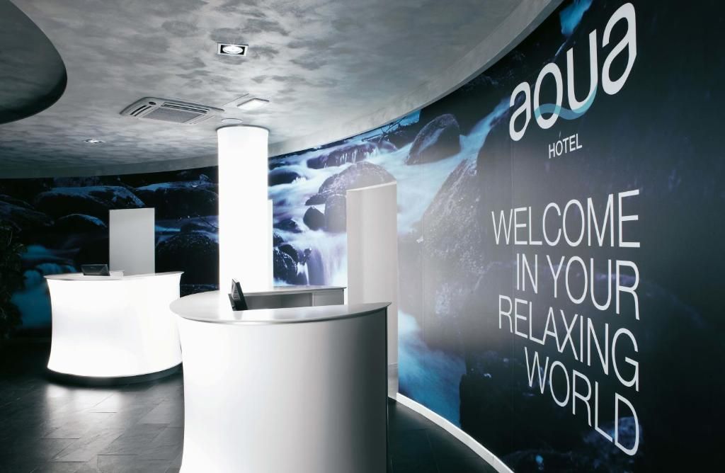 Un área de recepción de hotel moderna con una gran pantalla digital mostrando un mensaje de bienvenida y un telón de fondo de una cascada pintoresca.
