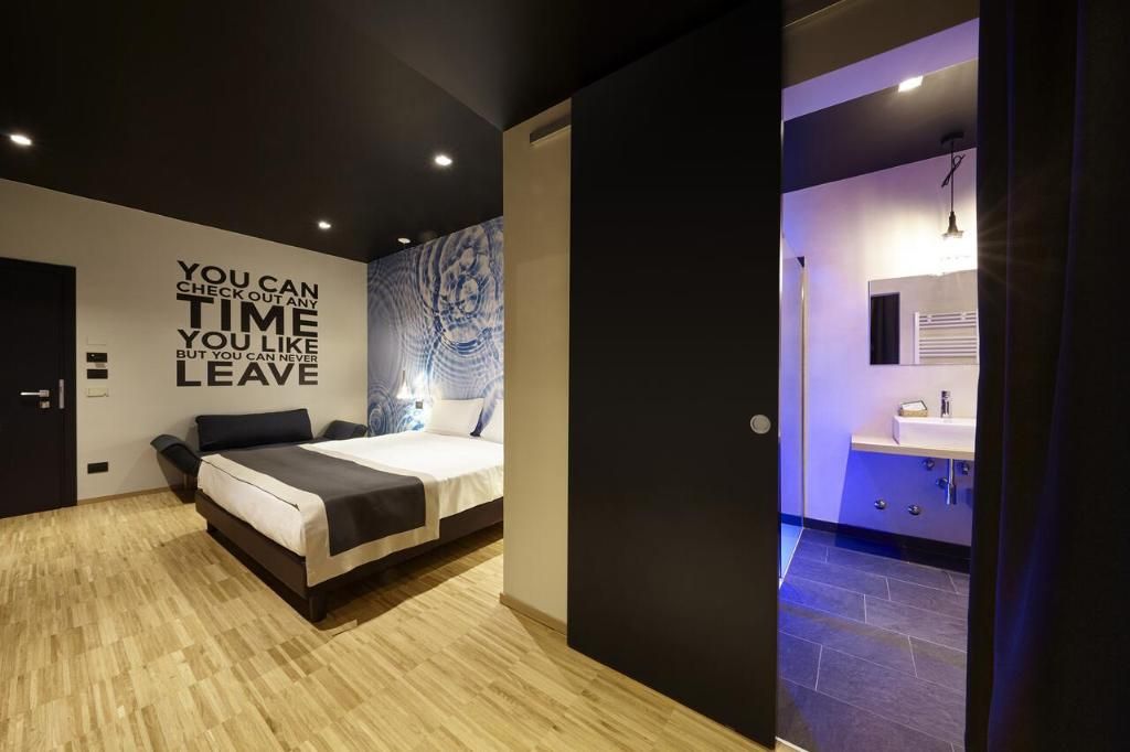 Quarto moderno com cama, parede com texto motivacional, banheiro com pia e espelho, e piso azulejado em azul.