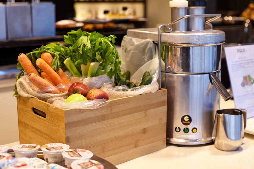 Una caja de madera con verduras frescas, una cafetera de acero inoxidable y una taza de metal sobre una encimera.