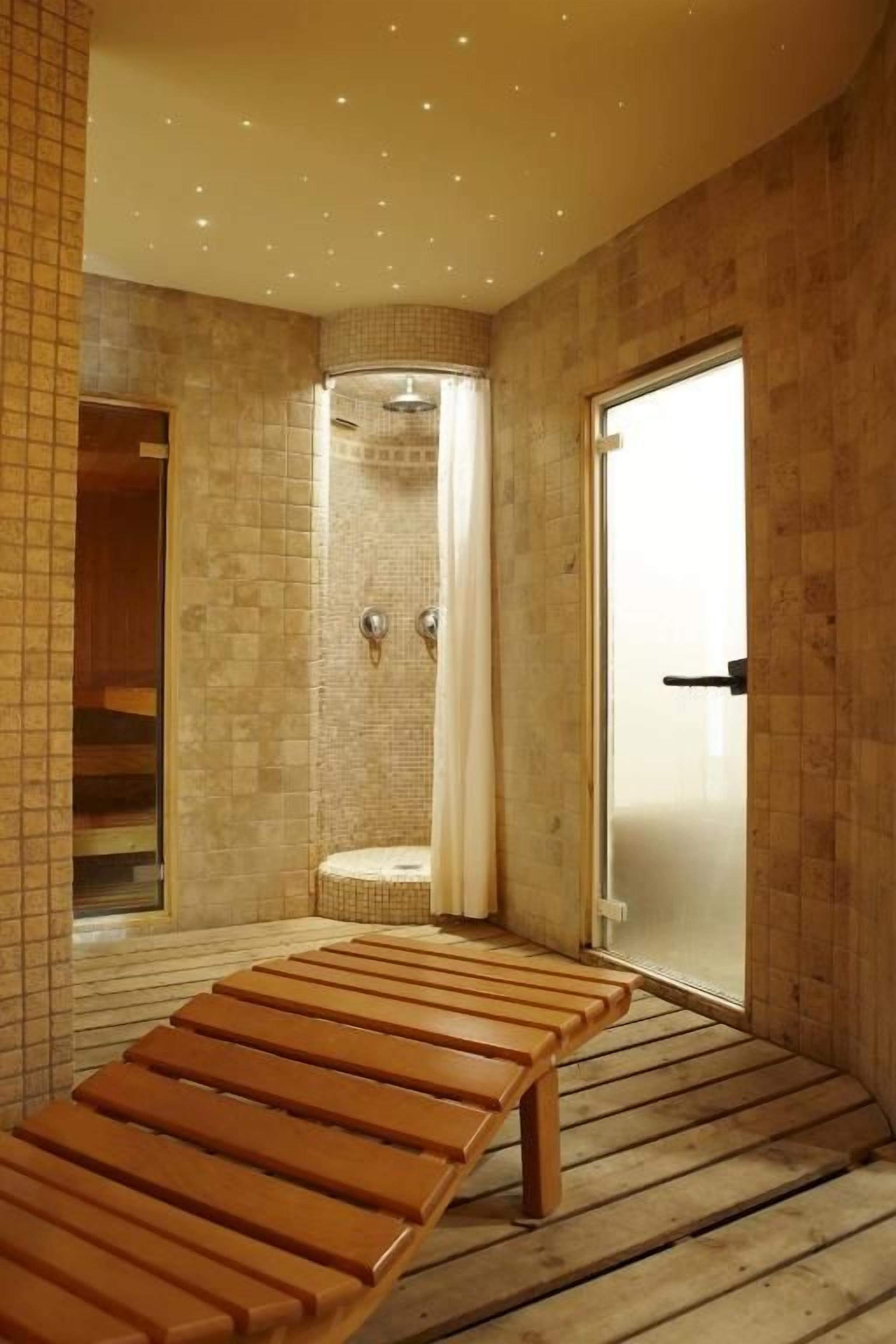 Habitación con un banco de madera, zona de ducha y una puerta.