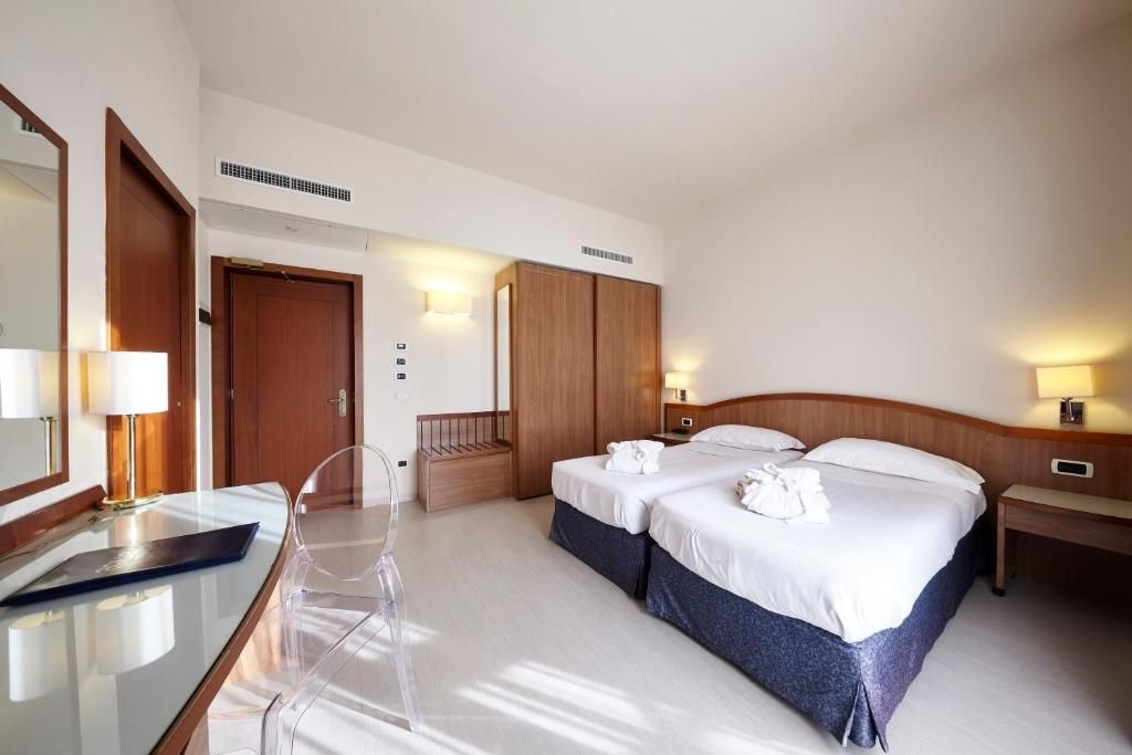 A hotel room with two beds, a desk with a chair, a mirror, and bedside lamps.