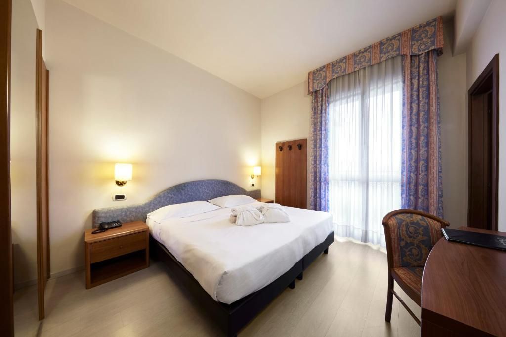 Una habitación de hotel con una cama, mesitas de noche, un escritorio y una silla.