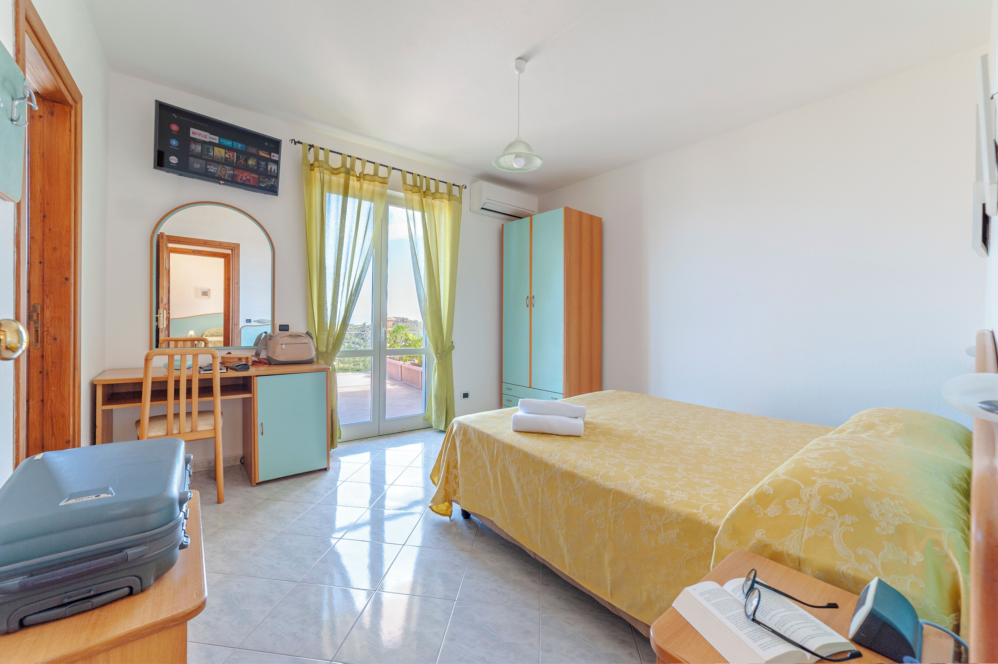 A hotel room with a bed, desk, chair, and a suitcase.