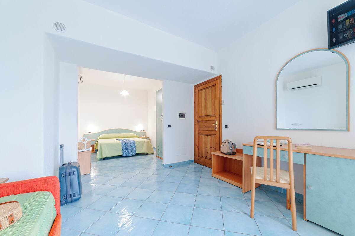 A room with a bed, a desk, a chair, a suitcase, and a TV mounted on the wall.