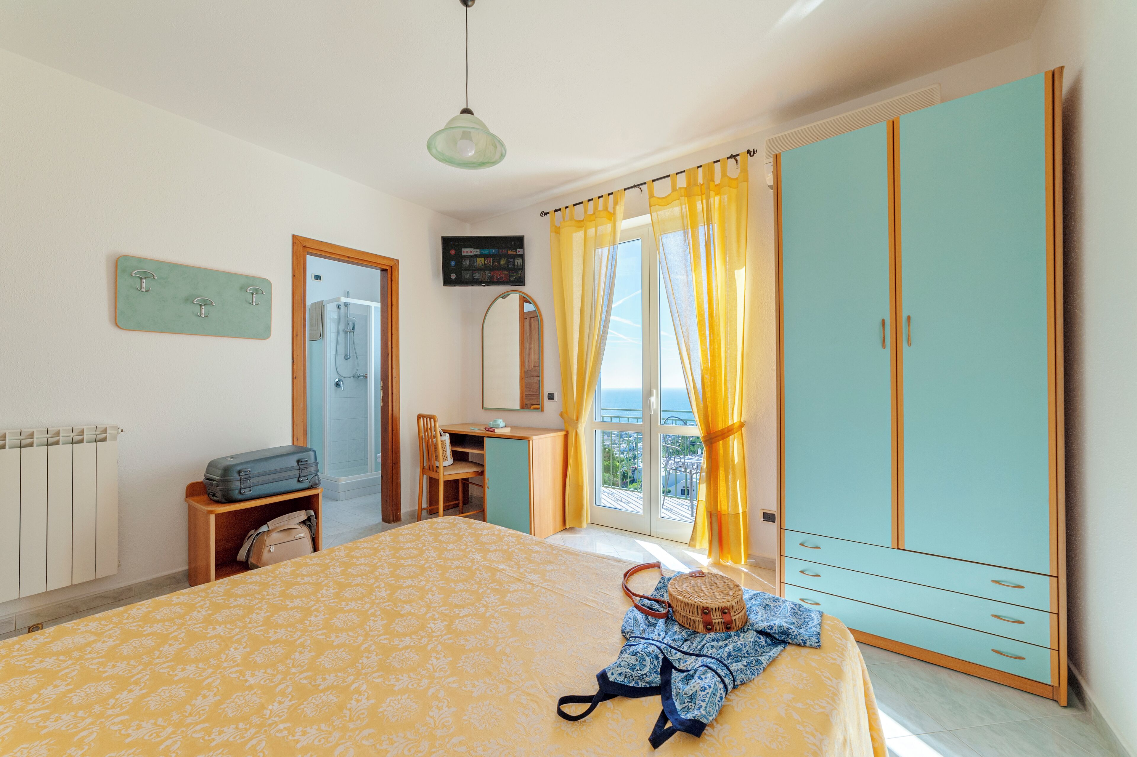 Un dormitorio con cama, escritorio, armario, ventana con cortinas y vistas al exterior.